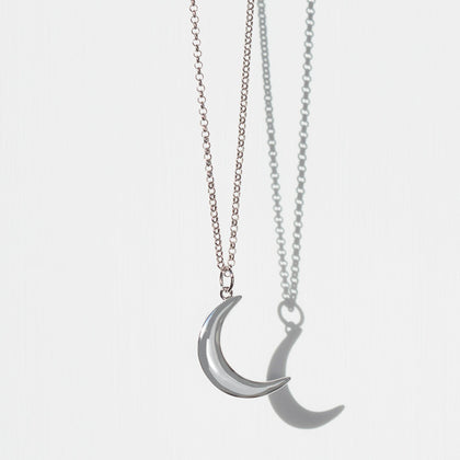 silver crescent moon charm on silver belcher chain necklace on plain white background with shadow